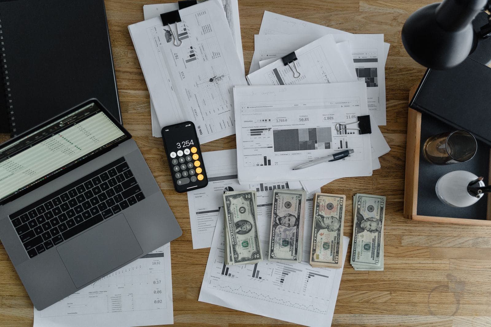 Overhead view of a desk with a laptop showing a spreadsheet, a calculator resting on a phone and printed financial reports