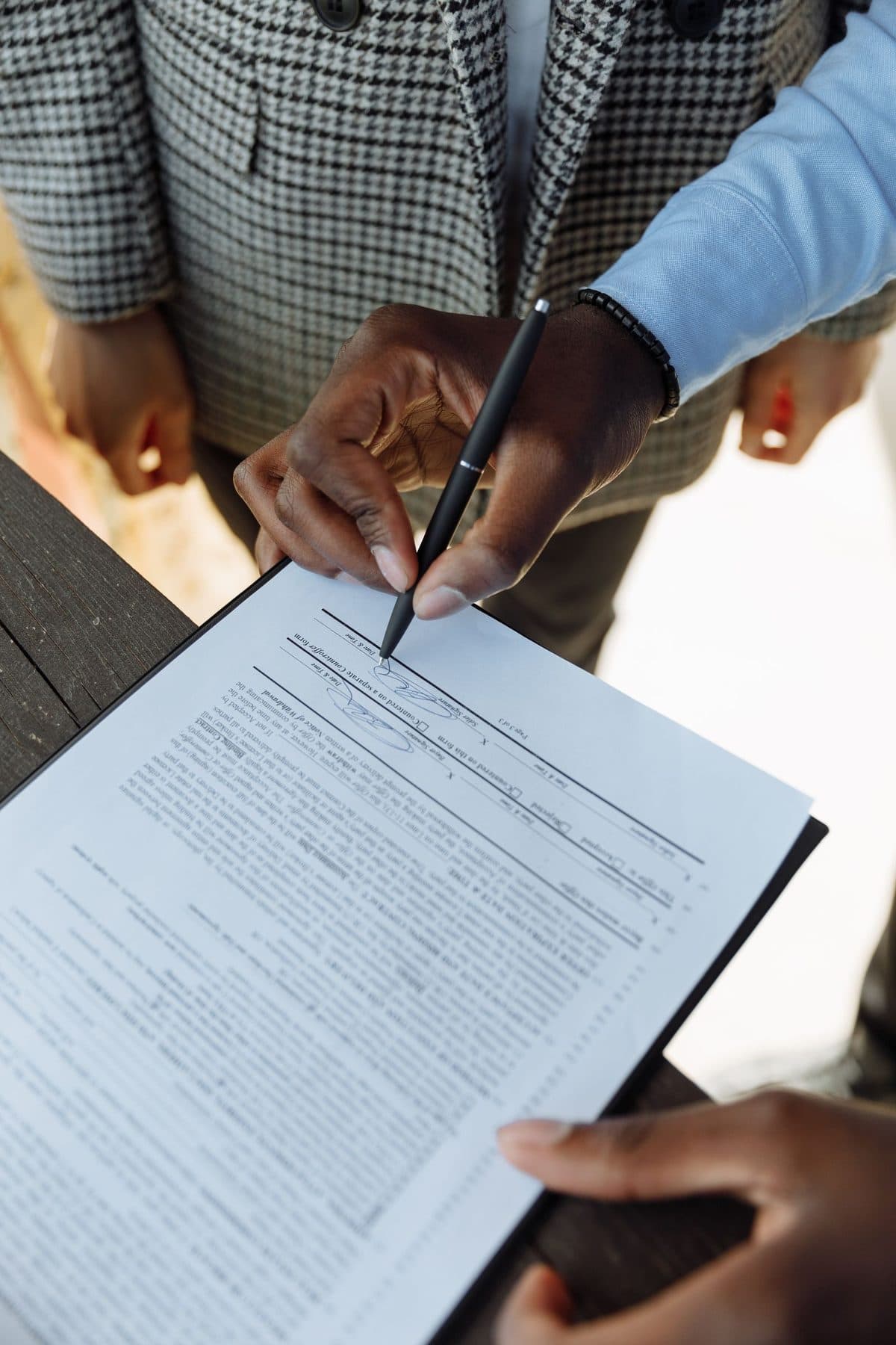 Close-up of two people signing a multi-clause contract held in a clipboard