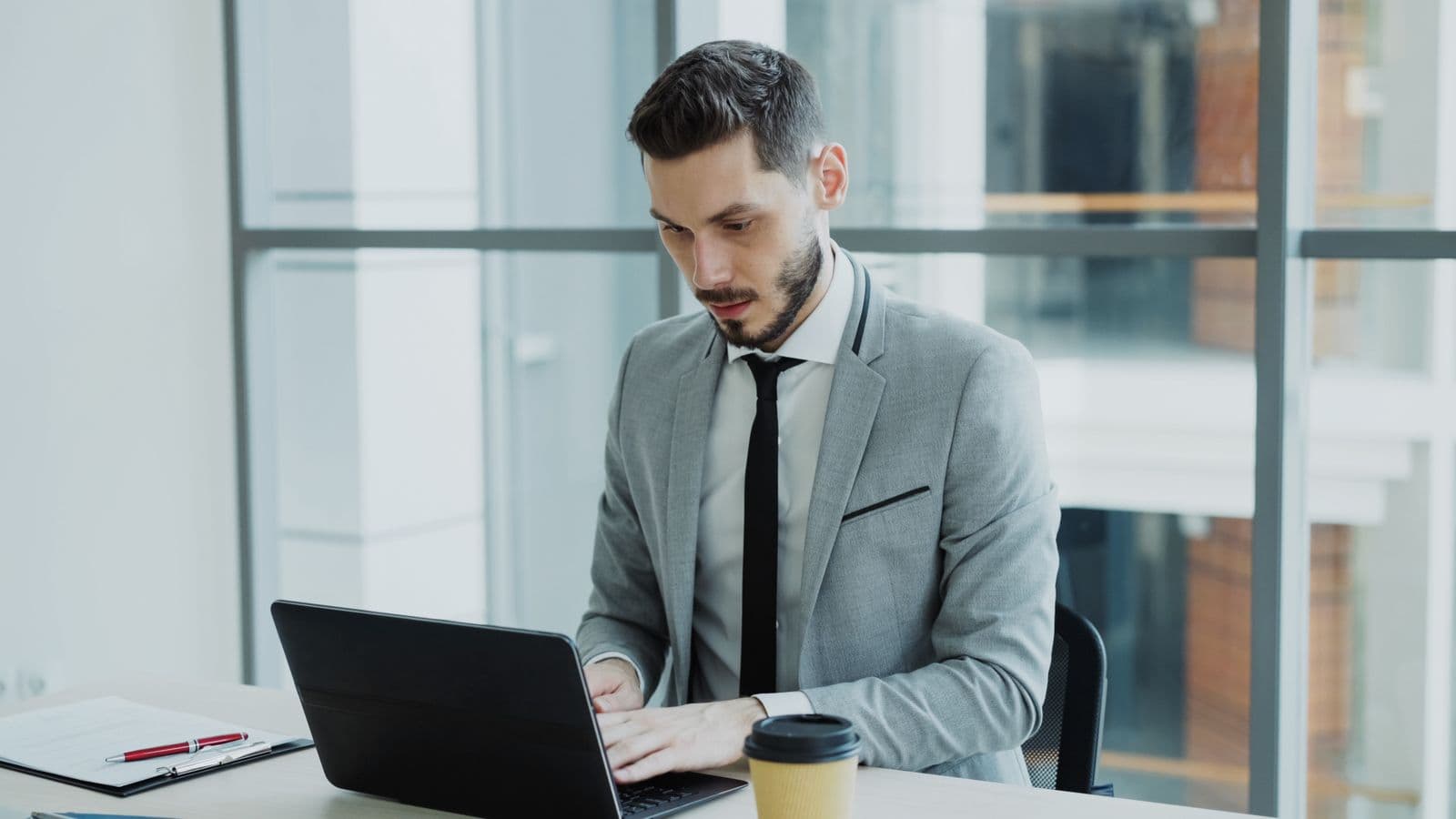 Office worker in a suit working on a laptop in a glass-walled office